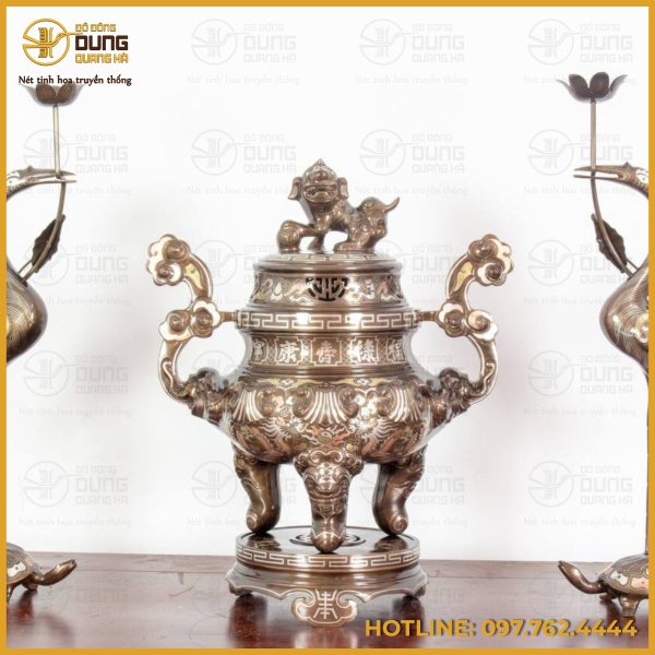 Bộ tam sự hạc bằng đồng gồm một đỉnh đồng đặt ở vị trí trung tâm, hai bên là đôi hạc chầu đối xứng. Thân đỉnh có dáng bầu tròn cân xứng, nắp đục thoáng hình chữ Thọ để khói trầm lan tỏa nhẹ nhàng, phía trên nắp là tượng nghê vờn cầu – biểu tượng của sự trấn an, giữ yên phúc trạch. Hai tai đỉnh được tạo dáng mây rồng uốn lượn, phần vai nối xuống bụng phủ đầy cánh sen, mây lửa và cụm phù điêu nổi, thể hiện bàn tay tài hoa của người nghệ nhân. Đỉnh đứng vững trên ba chân thú dáng lân, đặt trên bệ tròn nhiều tầng, tạo cảm giác bề thế và uy nghiêm trên mặt án gian thờ. Đôi hạc dáng thanh thoát, cổ vươn cao, mỏ ngậm đài sen dùng để đặt nến hoặc chén dầu, tượng trưng cho ánh sáng soi đường và sự thanh tịnh. Mỗi con hạc đứng trên lưng rùa, phía dưới là đế chạm hoa văn triện tinh xảo, tạo thành bố cục “song hạc chầu trung” hài hòa và trang trọng. Bộ đồ thờ được đúc thủ công hoàn toàn từ đồng nguyên chất, trải qua nhiều công đoạn như nấu luyện, tạo khuôn, đúc, sửa nguội và hoàn thiện bề mặt. Sau khi ra khuôn, từng chi tiết được gọt tỉa kỹ lưỡng để đường gờ, mép cánh, vảy lông và móng thú trở nên sắc nét, sống động. Thân đỉnh nổi bật với dải hồi văn triện chạy quanh, xen giữa là các chữ Phúc – Lộc – Thọ cùng họa tiết mây cuộn bay mềm mại. Nắp đỉnh được đục thủng vừa phải để khói trầm thoát đều, tạo cảm giác linh thiêng. Tượng nghê trên nắp được tách khối rõ ràng, từng chi tiết như bờm, vuốt và đuôi đều khắc tỉa sâu. Đôi hạc được chạm vảy lông nhỏ đều tay, phần sống lưng và cánh đánh nổi để phản chiếu ánh sáng; rùa có mai nổi, chân bám chắc vào đế, mang đến cảm giác chuyển động nhịp nhàng. Toàn bộ hệ hoa văn tuân theo mỹ thuật thờ Việt cổ, nhìn gần thấy độ sâu, nhìn xa lại liền khối đầy đặn. Màu sắc, Bộ tam sự mang gam đồng khảm tam khí truyền thống, nền chủ đạo là nâu trầm pha ánh xám và ánh oliu. Các gờ nổi như mép nắp, tai đỉnh, diềm sen và sống lông hạc được đánh bán bóng, phản chiếu ánh sáng dịu dưới ngọn đèn thờ. Một số chi tiết hoa văn được khảm tam khí tông sáng, giúp tôn lên vẻ sang trọng của chữ Thọ, hồi văn và đường viền, tạo điểm nhấn tinh tế mà không gây chói mắt. Phần chân thú và bệ đế giữ tông trầm để tăng chiều sâu thị giác, khiến tổng thể thêm vững và trang nhã. Qua thời gian thờ phụng, lớp màu đồng sẽ chuyển dần sang sắc trầm ấm, tạo vẻ cổ kính và linh thiêng, rất hợp với không gian thờ truyền thống Việt. Ý nghĩa của bộ tam sự hạc trong phong thủy Đỉnh đồng là trung tâm tiếp hương, nơi khói trầm quyện bay tượng trưng cho sợi dây gắn kết giữa cõi trần và tổ tiên. Tượng nghê trên nắp mang ý nghĩa trấn trạch, hóa giải điều dữ, bảo vệ gia đạo và giữ vững phúc lành. Ba chân thú gợi Tam tài Thiên – Địa – Nhân, trong khi bệ tròn biểu trưng cho sự viên mãn và trọn vẹn. Đôi hạc chầu là hình ảnh của sự thanh cao, trường thọ và tinh thần hướng thiện; hạc ngậm sen biểu trưng cho tâm trong sáng, sống thuận tự nhiên. Rùa tượng trưng cho bền vững và thọ mệnh dài lâu; thế hạc đứng trên rùa thể hiện sự hòa hợp âm dương, nâng đỡ vận khí và sự nghiệp cho gia chủ. Khi bài trí đủ bộ, tổng thể đạt thế “lưỡng long chầu nguyệt” cân đối, thể hiện nề nếp gia phong, trên dưới thuận hòa, con cháu hiếu kính và phúc lộc bền lâu.